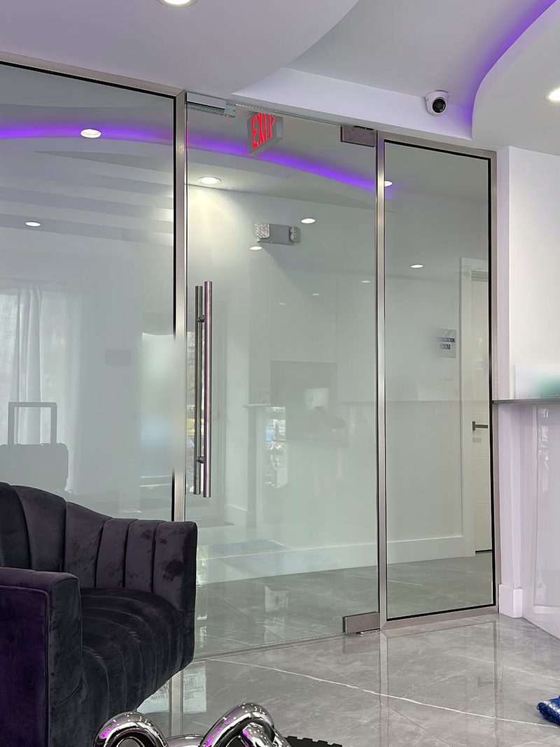 Clear glass entry doors and side panels with brushed stainless frames and a long pull handle in a reception area