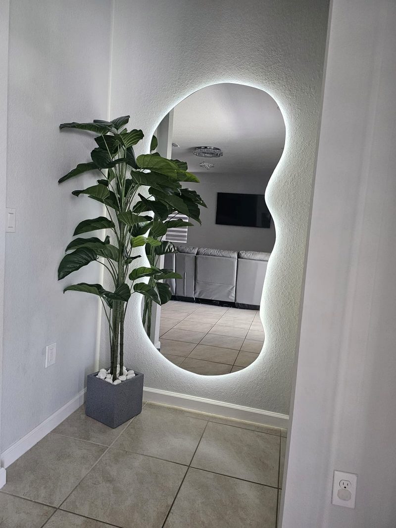 Wavy-shape full-length mirror with white LED backlight beside a potted plant