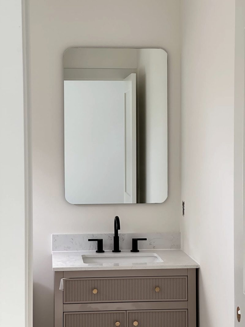 Rounded-corner frameless mirror above a fluted vanity with a matte black faucet