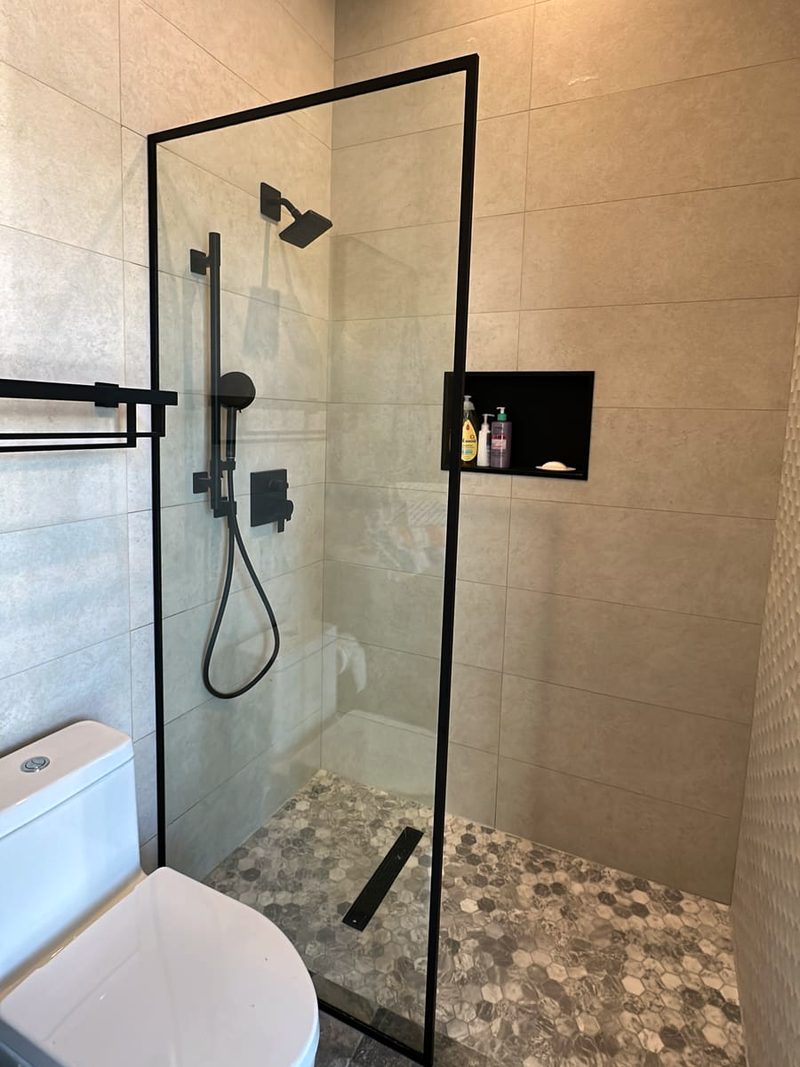 Fixed glass shower panel with a slim matte black frame in a walk-in shower with hexagon floor tile