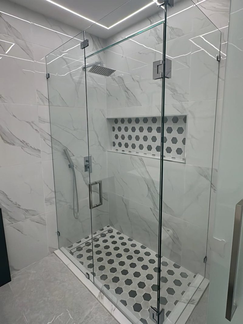 Frameless corner glass shower enclosure with chrome hinges and handle in a white marble-look bathroom