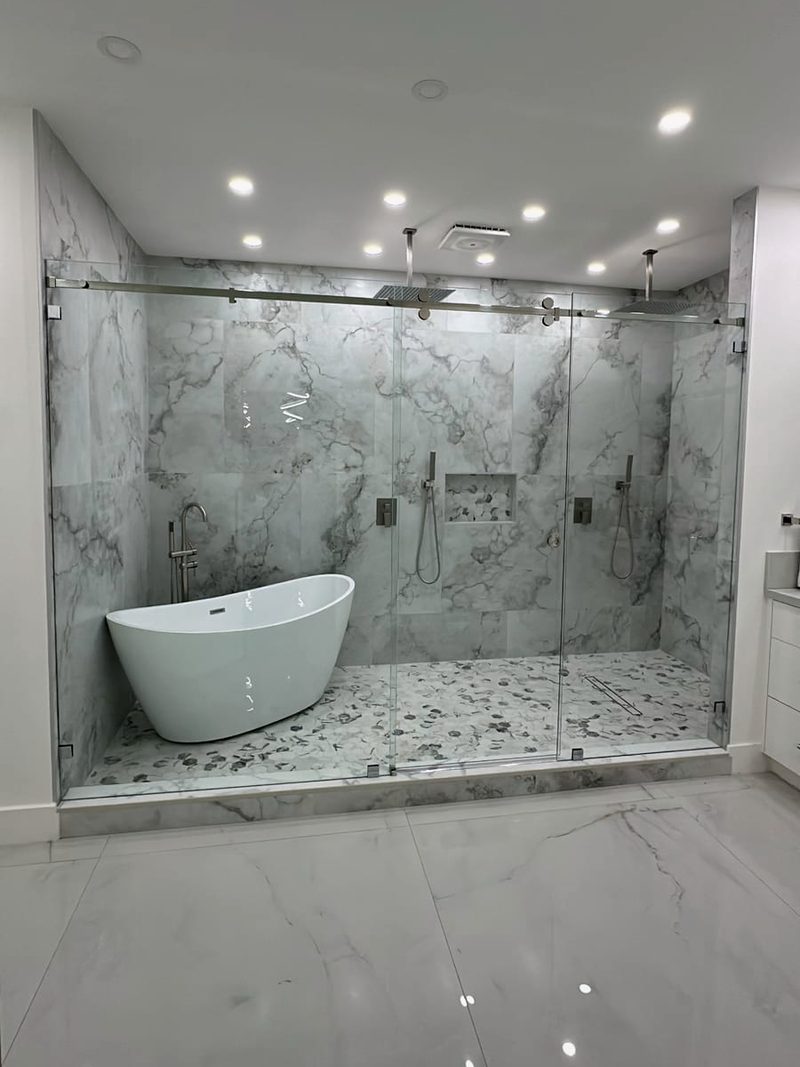 Wide frameless glass sliding enclosure spanning a wet room with a freestanding tub and two shower heads