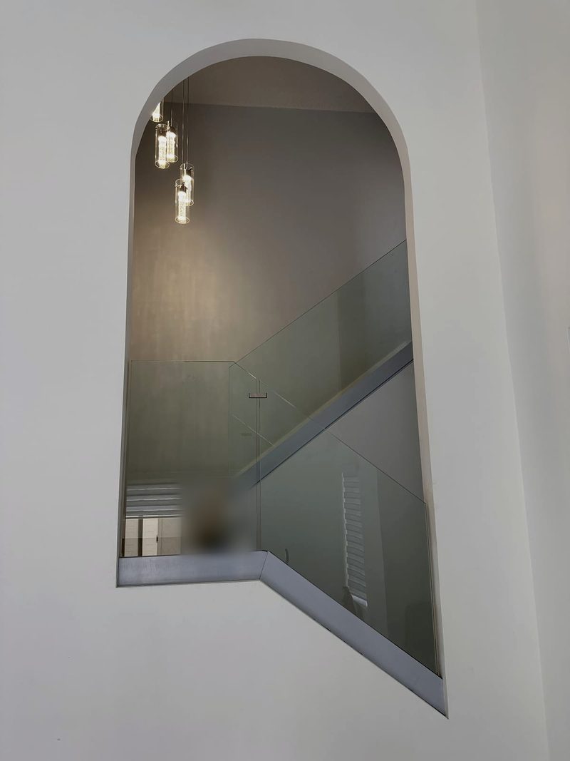 Frameless glass stair railing seen through an arched wall opening, with pendant lights above