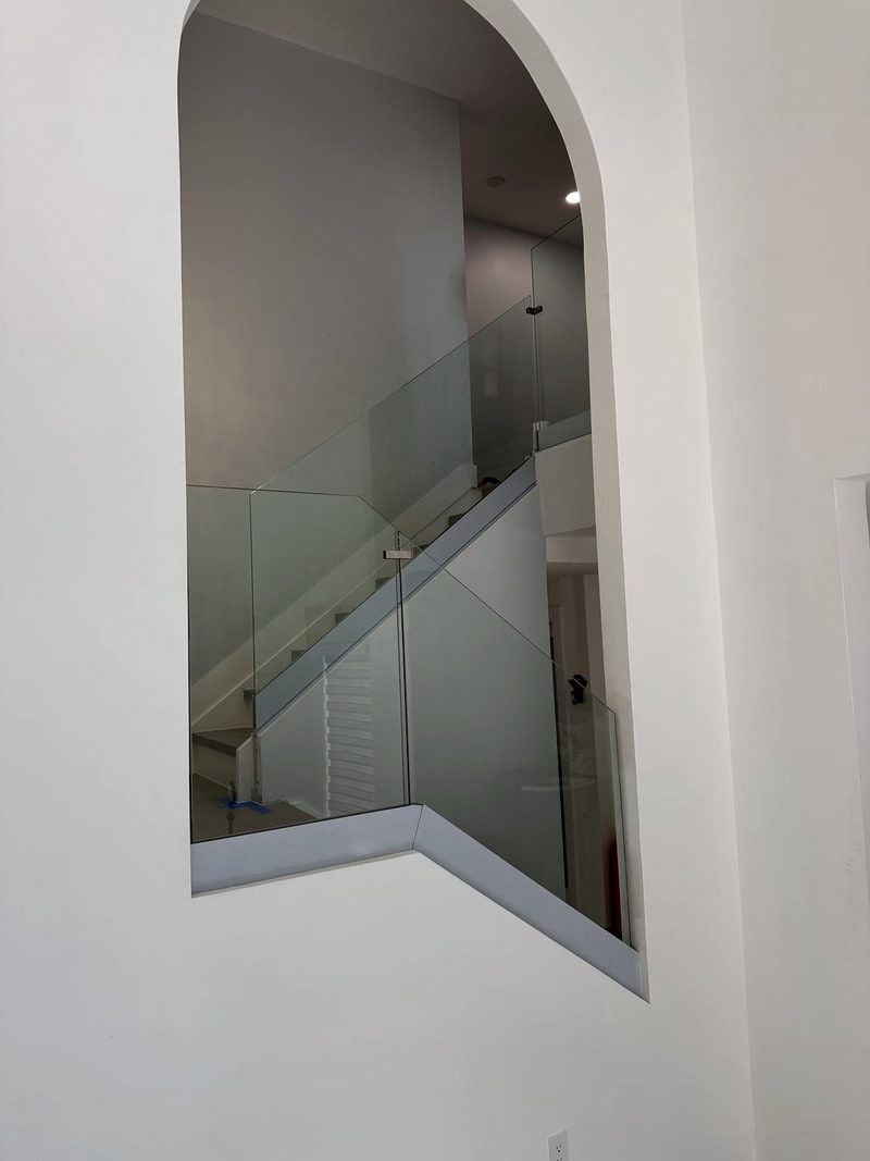 Frameless glass railing following a staircase, seen through an arched opening