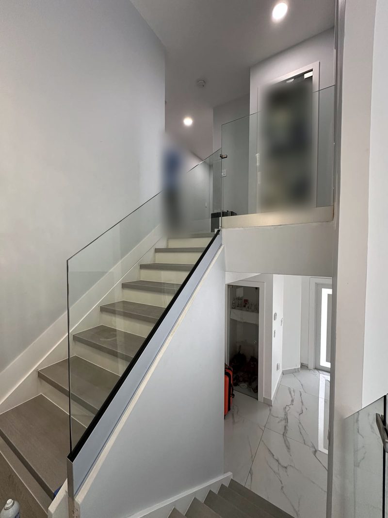 Frameless glass stair railing in a base shoe channel along a staircase with gray treads and a glass landing guard