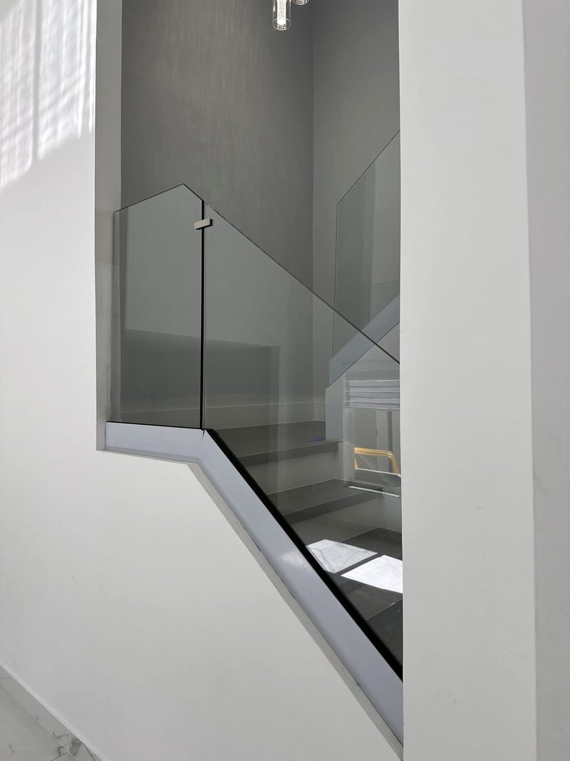 Close view of frameless glass railing panels with a stainless connector clip along a staircase opening